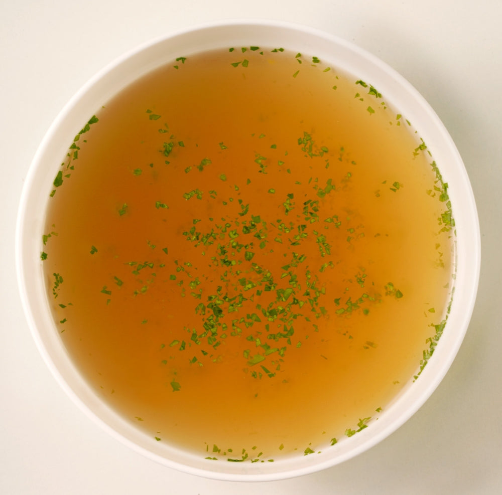 Warme Bio-Knochenbrühe mit Kräutern in einer weißen Schüssel, servierfertig angerichtet.