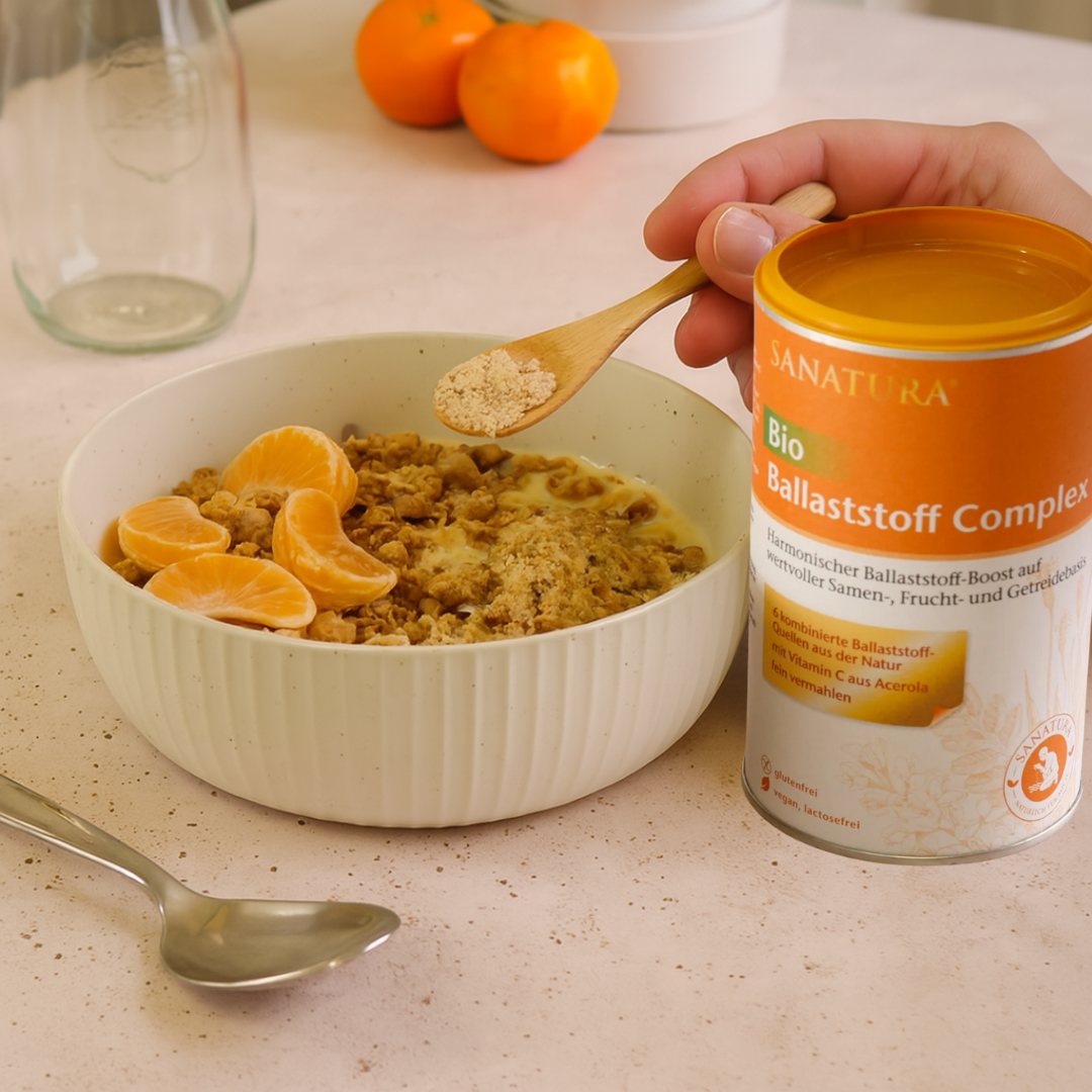 Sanatura Bio Ballaststoff Complex in Anwendung – Pulver wird mit Holzlöffel über Müsli mit Mandarinen gegeben, ballaststoffreicher Mix für Frühstück, Joghurt oder Shakes
