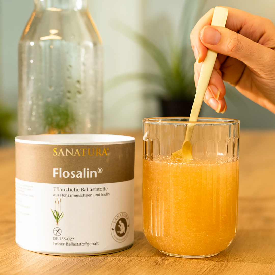 Sanatura Flosalin in der Anwendung – Glas mit angerührter Ballaststoffmischung wird mit Löffel umgerührt, daneben die geöffnete Dose mit Karaffe im Hintergrund
