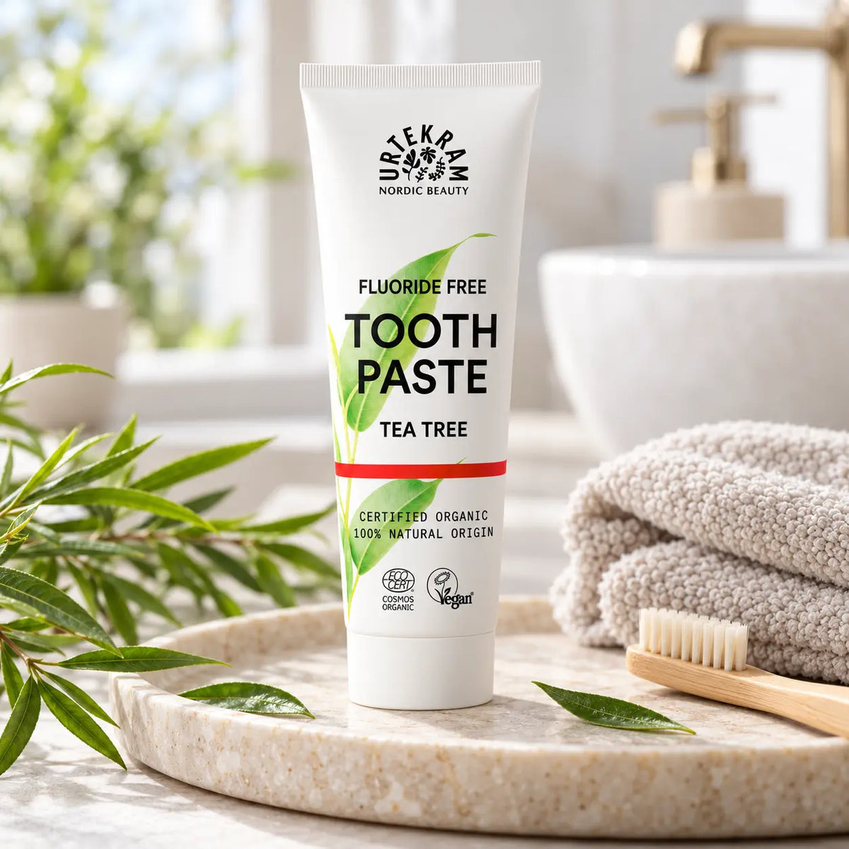 Urtekram Tea Tree Zahncreme im Badezimmer mit Bambuszahnbürste, Handtuch und grünen Pflanzen