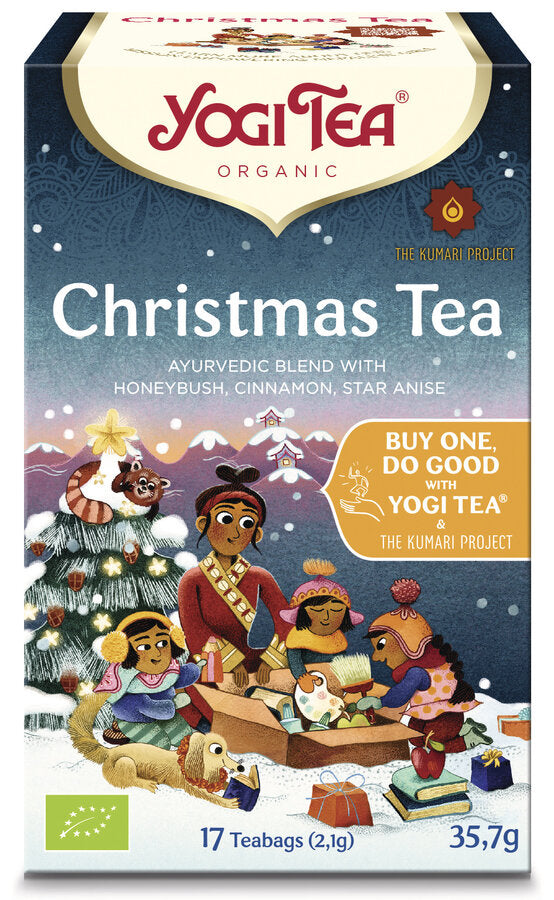 Eine Packung des 'Christmas Tea' von Yogi Tea. Die Verpackung ist farbenfroh gestaltet und zeigt eine Illustration einer Familie, die Geschenke unter einem geschmückten Weihnachtsbaum öffnet. Oben steht in roter Schrift 'Yogi Tea' und darunter 'Organic'. Die Teesorte ist als 'Ayurvedic blend with honeybush, cinnamon, star anise' beschrieben. Auf der rechten Seite befindet sich ein gelbes Feld mit der Aufschrift 'Buy one, do good with Yogi Tea & The Kumari Project'. Unten links ist das europäische Bio-Siegel