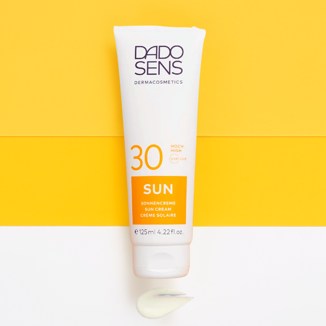 DADO SENS SUN Sonnencreme LSF 30 – stylisches Produktbild auf zweifarbigem Hintergrund, mit Cremeauftrag