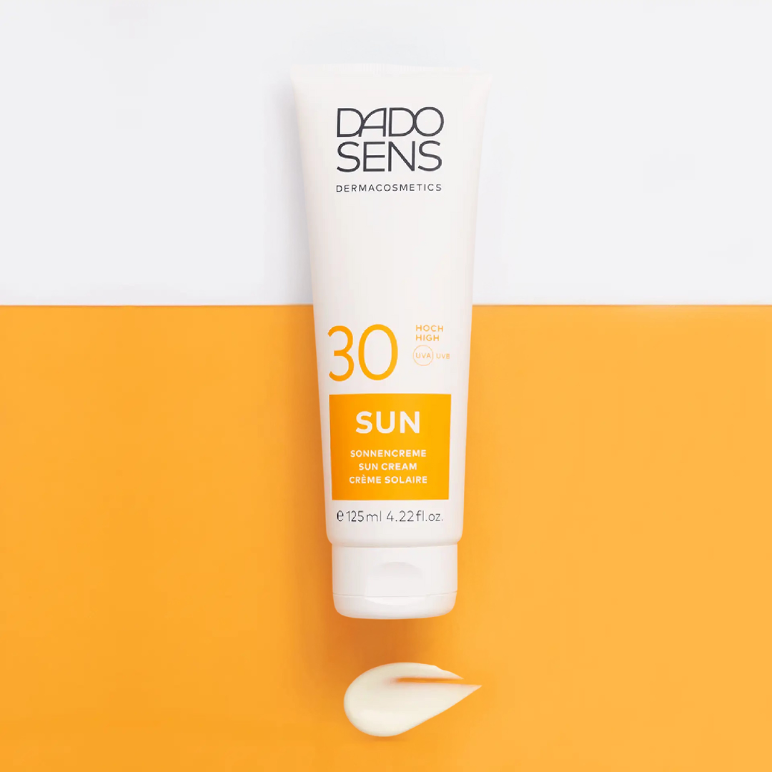 DADO SENS SUN Sonnencreme LSF 30 – Sonnenpflege in Szene gesetzt auf orange-weißem Hintergrund, Tube mit Textur