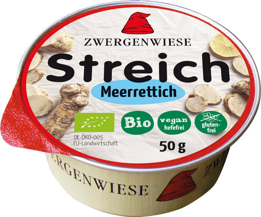 Das Bild zeigt eine runde Dose des veganen Brotaufstrichs "Streich Meerrettich" von Zwergenwiese. Die Dose hat einen roten Deckelrand und eine weiße Oberseite mit der Aufschrift "Zwergenwiese Streich Meerrettich". Es gibt Symbole, die das Produkt als bio, vegan (hefefrei) und glutenfrei kennzeichnen. Die Nettofüllmenge beträgt 50 Gramm. Auf dem Deckel sind außerdem Abbildungen von Meerrettich und Zitronenscheiben zu sehen. Das Markensymbol, ein roter Zwergenhut, ist ebenfalls auf dem Deckel abgebildet.