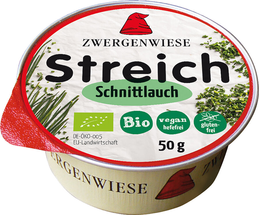 Das Bild zeigt eine runde Dose des veganen Brotaufstrichs "Streich Schnittlauch" von Zwergenwiese. Die Dose hat einen roten Deckelrand und eine weiße Oberseite mit der Aufschrift "Zwergenwiese Streich Schnittlauch". Es gibt Symbole, die das Produkt als bio, vegan (hefefrei) und glutenfrei kennzeichnen. Die Nettofüllmenge beträgt 50 Gramm. Auf dem Deckel sind außerdem Abbildungen von frischem Schnittlauch zu sehen. Das Markensymbol, ein roter Zwergenhut, ist ebenfalls auf dem Deckel abgebildet.