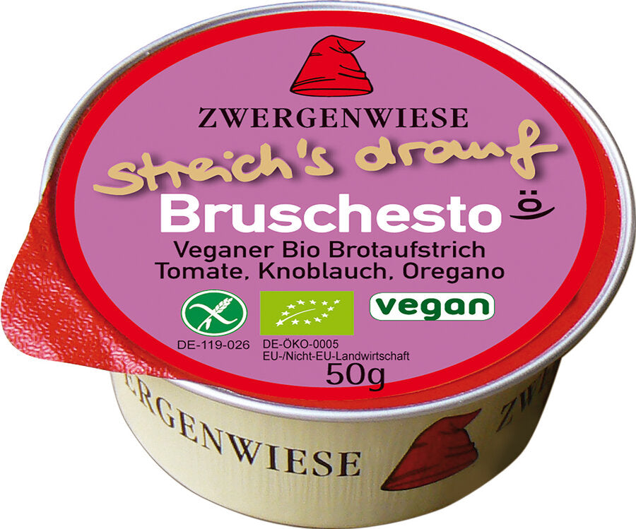 Das Bild zeigt eine runde, vegane Brotaufstrich-Dose der Marke Zwergenwiese. Die Dose hat einen roten Deckelrand und eine pinkfarbene Oberseite mit der Aufschrift "streich's drauf Bruscheto". Unterhalb des Produktnamens steht "Veganer Bio Brotaufstrich Tomate, Knoblauch, Oregano". Es gibt auch Symbole, die das Produkt als vegan und bio-zertifiziert kennzeichnen. Die Nettofüllmenge beträgt 50 Gramm. Das Markensymbol, ein roter Zwergenhut, ist ebenfalls auf dem Deckel abgebildet.