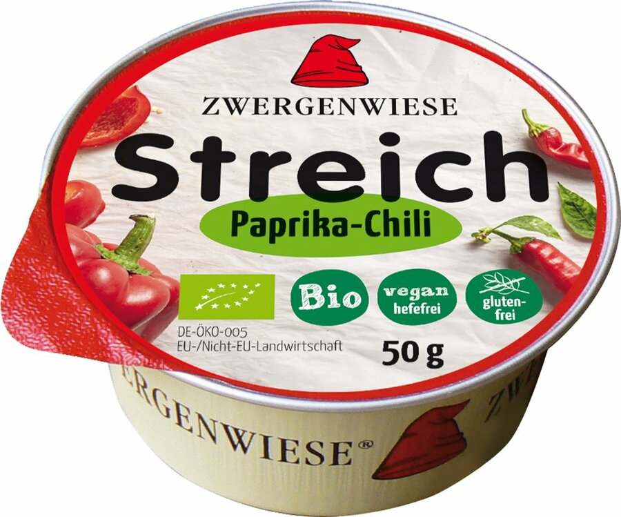 Das Bild zeigt eine runde Dose des veganen Brotaufstrichs "Streich Paprika-Chili" von Zwergenwiese. Die Dose hat einen roten Deckelrand und eine weiße Oberseite mit der Aufschrift "Zwergenwiese Streich Paprika-Chili". Es gibt Symbole, die das Produkt als bio, vegan (hefefrei) und glutenfrei kennzeichnen. Die Nettofüllmenge beträgt 50 Gramm. Auf dem Deckel sind außerdem Abbildungen von Paprika und Chili zu sehen. Das Markensymbol, ein roter Zwergenhut, ist ebenfalls auf dem Deckel abgebildet.