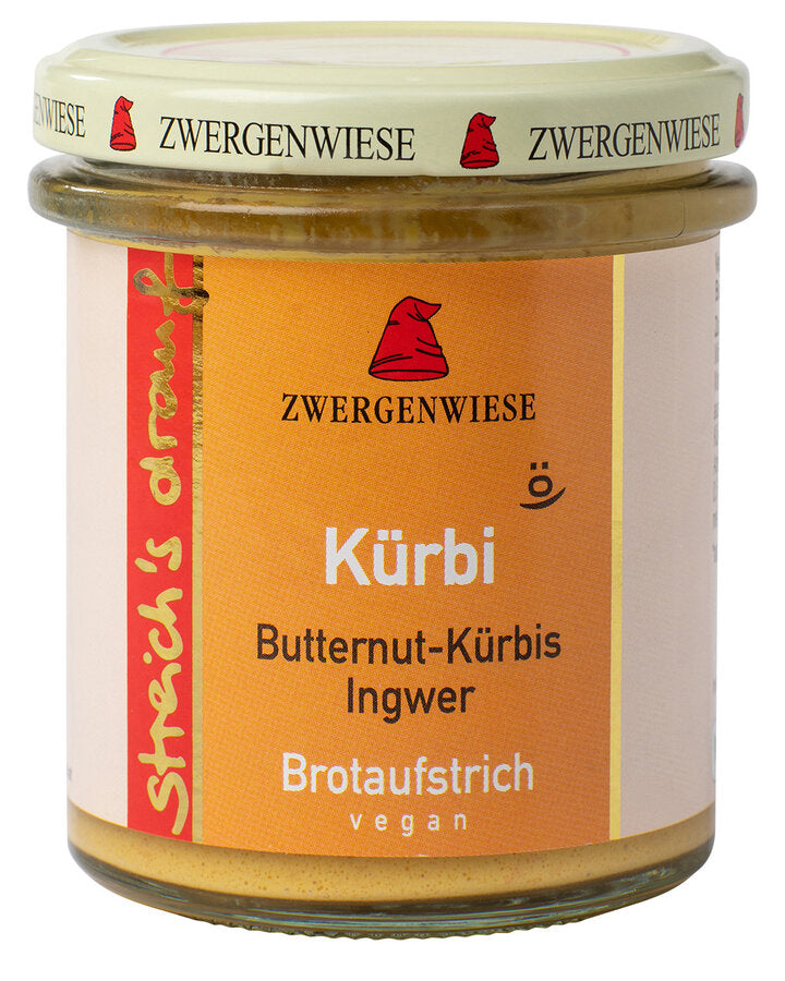 Das Bild zeigt ein Glas des veganen Brotaufstrichs "Kürbi" der Marke Zwergenwiese. Der Deckel des Glases ist beige mit dem Zwergenwiese-Logo, einem roten Zwergenhut, und der Aufschrift "Zwergenwiese" auf dem Rand. Das Etikett des Glases ist orange und zeigt oben das Zwergenwiese-Logo, darunter den Produktnamen "Kürbi" in weißer Schrift, gefolgt von den Zutaten "Butternut-Kürbis Ingwer". Unten steht "Brotaufstrich vegan" ebenfalls in weißer Schrift.