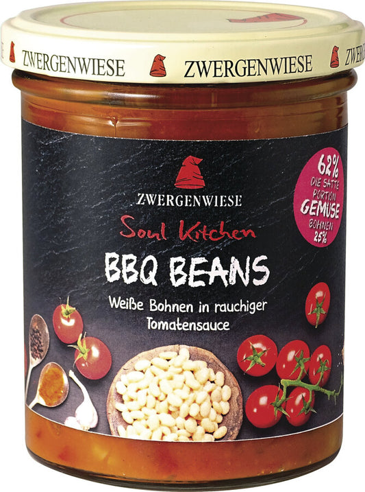 Das Bild zeigt ein Glas "BBQ Beans" von Zwergenwiese aus der "Soul Kitchen" Reihe. Der Deckel ist beige mit einem roten Zwergenhut. Das Etikett ist schwarz und zeigt die Aufschrift "Zwergenwiese Soul Kitchen BBQ Beans" in weißer und roter Schrift. Darunter steht "Weiße Bohnen in rauchiger Tomatensauce". Auf dem Etikett sind außerdem Abbildungen von Kirschtomaten, weißen Bohnen und Gewürzen zu sehen. Ein rotes Siegel auf dem Etikett weist auf einen 62% Gemüseanteil hin, davon 25% Bohnen.