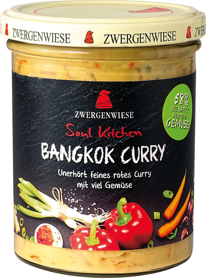 Das Bild zeigt ein Glas "Bangkok Curry" von Zwergenwiese aus der "Soul Kitchen" Reihe. Der Deckel ist beige mit einem roten Zwergenhut. Das Etikett ist schwarz und zeigt die Aufschrift "Zwergenwiese Soul Kitchen Bangkok Curry" in weißer und roter Schrift. Darunter steht "Unerhört feines rotes Curry mit viel Gemüse". Auf dem Etikett sind außerdem Abbildungen von Paprika, Karotten und Frühlingszwiebeln zu sehen. Ein grünes Siegel auf dem Etikett weist auf einen 58% Gemüseanteil hin.