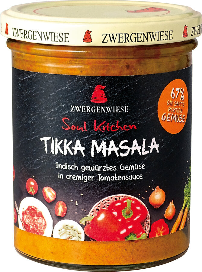 Das Bild zeigt ein Glas "Tikka Masala" von Zwergenwiese aus der "Soul Kitchen" Reihe. Der Deckel ist beige mit einem roten Zwergenhut. Das Etikett ist schwarz und zeigt die Aufschrift "Zwergenwiese Soul Kitchen Tikka Masala" in weißer und roter Schrift. Darunter steht "Indisch gewürztes Gemüse in cremiger Tomatensauce". Auf dem Etikett sind außerdem Abbildungen von Paprika, Tomaten, Zwiebeln und anderen Gemüsesorten zu sehen. Ein oranges Siegel auf dem Etikett weist auf einen 67% Gemüseanteil hin.