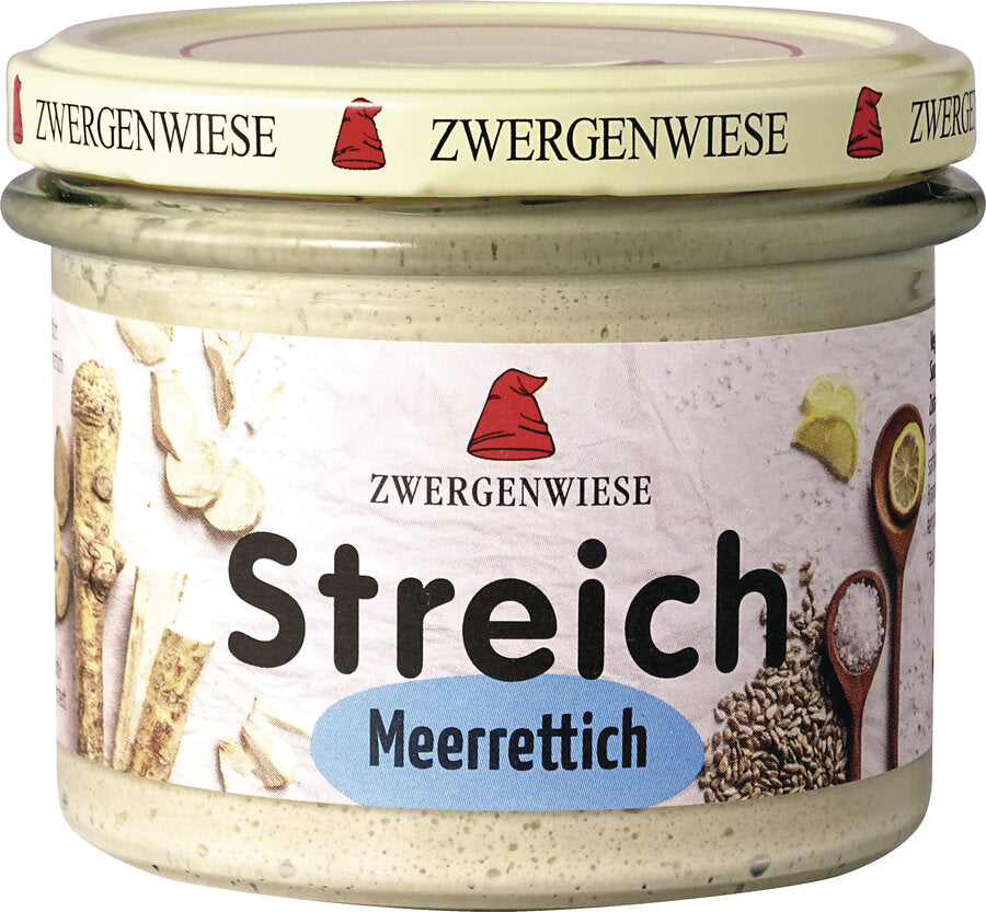 Das Bild zeigt ein Glas des veganen Brotaufstrichs "Streich Meerrettich" von Zwergenwiese. Der Deckel ist beige mit einem roten Zwergenhut. Das Etikett ist weiß mit Abbildungen von Meerrettich und Zitronenscheiben. In der Mitte steht "Zwergenwiese Streich Meerrettich" in schwarzer und blauer Schrift.