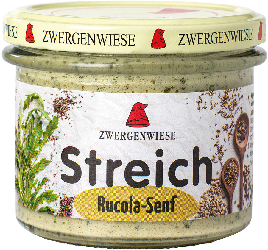 Das Bild zeigt ein Glas des veganen Brotaufstrichs "Streich Rucola-Senf" von Zwergenwiese. Der Deckel ist beige mit einem roten Zwergenhut. Das Etikett ist weiß mit Abbildungen von Rucola und Senfkörnern. In der Mitte steht "Zwergenwiese Streich Rucola-Senf" in schwarzer und gelber Schrift.