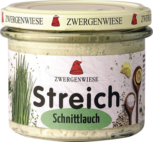 Das Bild zeigt ein Glas des veganen Brotaufstrichs "Streich Schnittlauch" von Zwergenwiese. Der Deckel ist beige mit einem roten Zwergenhut. Das Etikett ist weiß mit Abbildungen von frischem Schnittlauch, Zitronenscheiben und Gewürzen. In der Mitte steht "Zwergenwiese Streich Schnittlauch" in schwarzer und grüner Schrift.