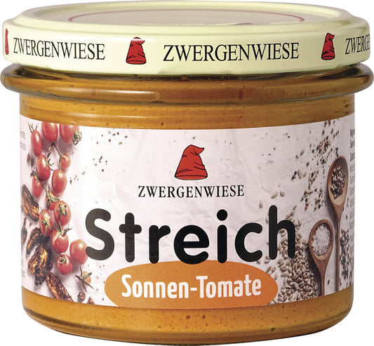 Das Bild zeigt ein Glas des veganen Brotaufstrichs "Streich Sonnen-Tomate" von Zwergenwiese. Der Deckel ist beige mit einem roten Zwergenhut. Das Etikett ist weiß mit Abbildungen von getrockneten Tomaten, frischen Tomaten und Gewürzen. In der Mitte steht "Zwergenwiese Streich Sonnen-Tomate" in schwarzer und orangefarbener Schrift.