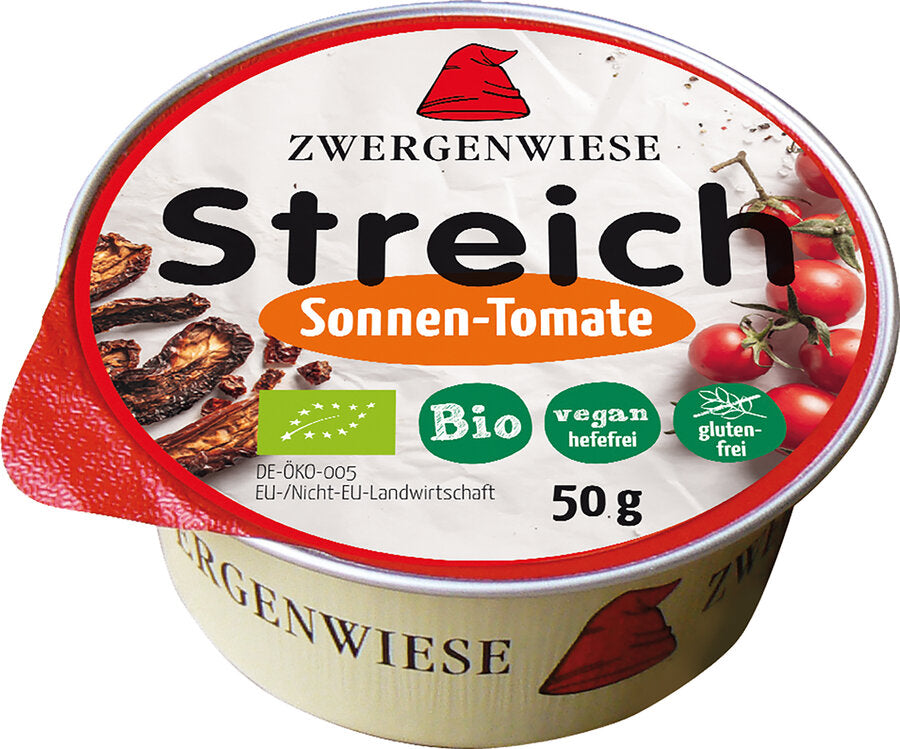 Das Bild zeigt eine runde Dose des veganen Brotaufstrichs "Streich Sonnen-Tomate" von Zwergenwiese. Die Dose hat einen roten Deckelrand und eine weiße Oberseite mit der Aufschrift "Zwergenwiese Streich Sonnen-Tomate". Es gibt Symbole, die das Produkt als bio, vegan (hefefrei) und glutenfrei kennzeichnen. Die Nettofüllmenge beträgt 50 Gramm. Auf dem Deckel sind außerdem Abbildungen von getrockneten Tomaten und frischen Tomaten zu sehen.