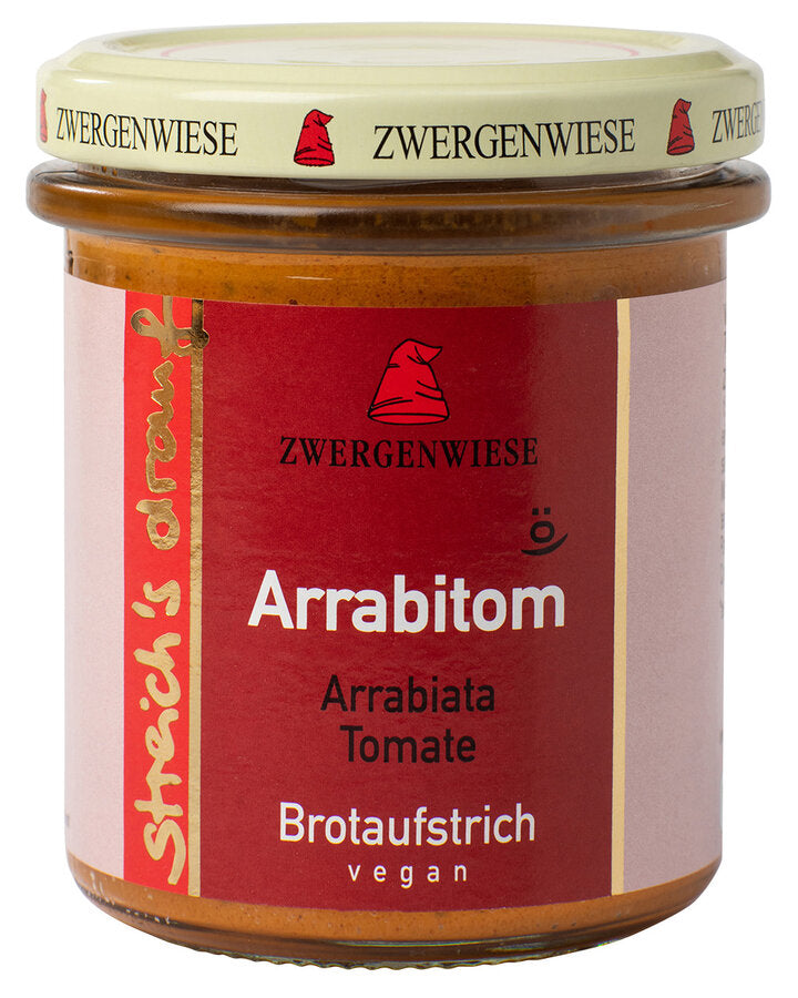 Das Bild zeigt ein Glas "Arrabitom" Brotaufstrich von Zwergenwiese. Der Deckel ist beige mit einem roten Zwergenhut. Das Etikett ist rot und zeigt die Aufschrift "Zwergenwiese Arrabitom" in weißer und schwarzer Schrift. Darunter steht "Arrabiata Tomate". An der Seite des Etiketts steht "Streich's drauf" in gelber Schrift auf rotem Hintergrund. Der Brotaufstrich ist vegan.