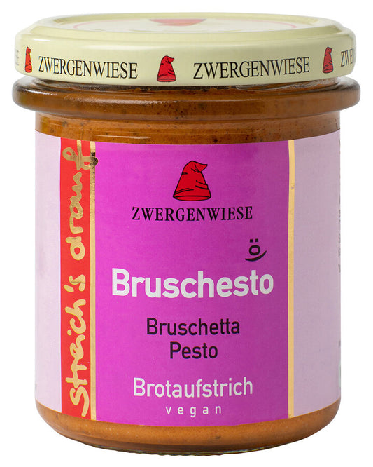 Das Bild zeigt ein Glas "Bruschesto" Brotaufstrich von Zwergenwiese. Der Deckel ist beige mit einem roten Zwergenhut. Das Etikett ist lila und zeigt die Aufschrift "Zwergenwiese Bruschesto" in weißer Schrift. Darunter steht "Bruschetta Pesto". An der Seite des Etiketts steht "Streich's drauf" in gelber Schrift auf rotem Hintergrund. Der Brotaufstrich ist vegan.