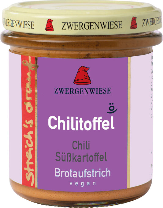 Das Bild zeigt ein Glas "Chilitoffel" Brotaufstrich von Zwergenwiese. Der Deckel ist beige mit einem roten Zwergenhut. Das Etikett ist lila und zeigt die Aufschrift "Zwergenwiese Chilitoffel" in weißer Schrift. Darunter steht "Chili Süßkartoffel". An der Seite des Etiketts steht "Streich's drauf" in gelber Schrift auf rotem Hintergrund. Der Brotaufstrich ist vegan.