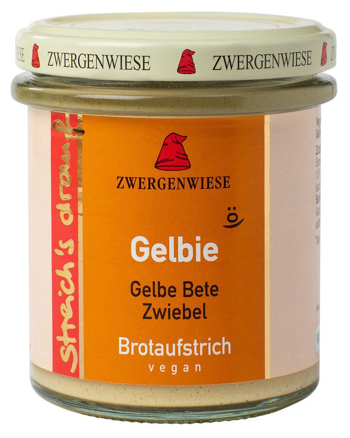 Das Bild zeigt ein Glas "Gelbie" Brotaufstrich von Zwergenwiese. Der Deckel ist beige mit einem roten Zwergenhut. Das Etikett ist orange und zeigt die Aufschrift "Zwergenwiese Gelbie" in weißer Schrift. Darunter steht "Gelbe Bete Zwiebel". An der Seite des Etiketts steht "Streich's drauf" in gelber Schrift auf rotem Hintergrund. Der Brotaufstrich ist vegan.