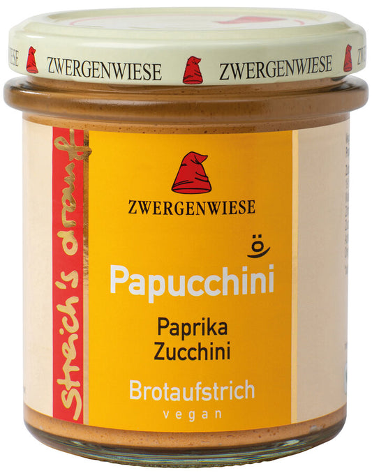 Das Bild zeigt ein Glas "Papucchini" Brotaufstrich von Zwergenwiese. Der Deckel ist beige mit roten Zwergenhüten. Das Etikett ist orange und zeigt die Aufschrift "Zwergenwiese Papucchini" in weißer Schrift. Darunter steht "Paprika Zucchini". An der Seite des Etiketts steht "Streich's drauf" in gelber Schrift auf rotem Hintergrund. Der Brotaufstrich ist vegan.