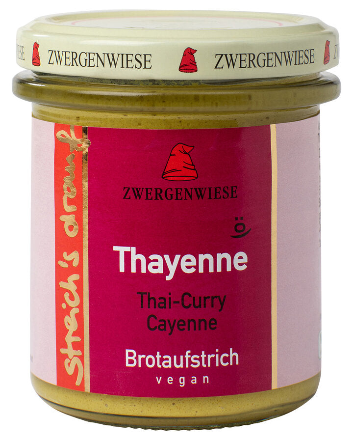 Das Bild zeigt ein Glas "Thayenne" Brotaufstrich von Zwergenwiese. Der Deckel ist beige mit roten Zwergenhüten. Das Etikett ist pink und zeigt die Aufschrift "Zwergenwiese Thayenne" in weißer Schrift. Darunter steht "Thai-Curry Cayenne". An der Seite des Etiketts steht "Streich's drauf" in gelber Schrift auf rotem Hintergrund. Der Brotaufstrich ist vegan.