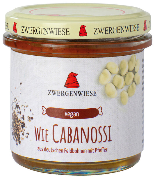 Ein Glas mit dem veganen Aufstrich "Wie Cabanossi" von der Marke Zwergenwiese. Das Etikett zeigt eine rote Zwergenmütze und die Aufschrift "Wie Cabanossi - aus deutschen Feldbohnen mit Pfeffer". Abgebildet sind Pfefferkörner und Feldbohnen, die die Zutaten und den würzigen Geschmack des Aufstrichs hervorheben. Der beige Deckel trägt mehrfach das Zwergenwiese-Logo.