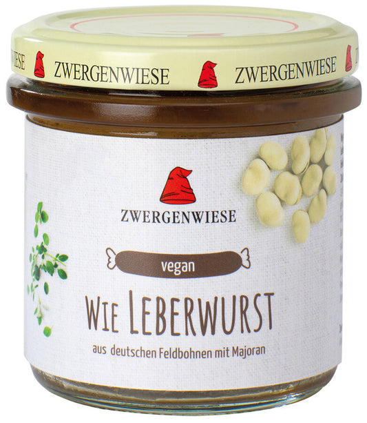 Ein Glas mit dem veganen Aufstrich "Wie Leberwurst" von der Marke Zwergenwiese. Das Etikett zeigt eine rote Zwergenmütze und die Aufschrift "Wie Leberwurst - aus deutschen Feldbohnen mit Majoran". Abgebildet sind Feldbohnen und Majoranblätter, die die Zutaten und den aromatischen Geschmack des Aufstrichs hervorheben. Der beige Deckel trägt mehrfach das Zwergenwiese-Logo.