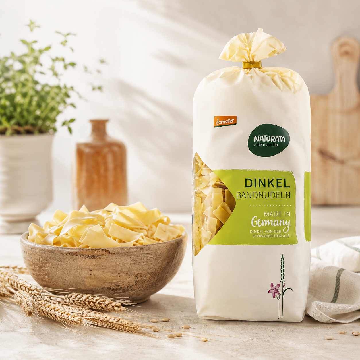 Naturata Dinkel-Bandnudeln neben einer Schale mit ungekochten Bandnudeln in heller Küche