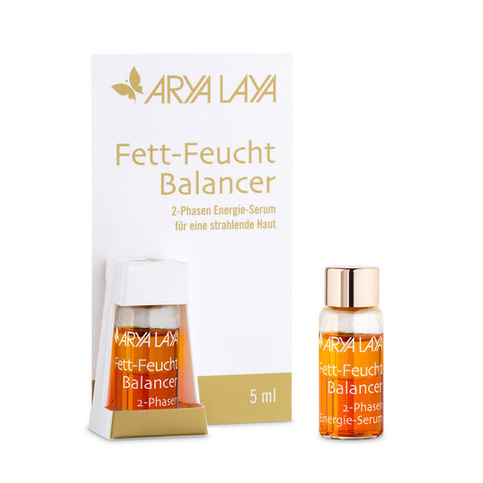 Arya Laya Fett-Feucht Balancer 2-Phasen Energie-Serum in einer 5-ml-Miniaturflasche mit goldfarbenem Deckel. Die Verpackung ist weiß mit goldener Schrift. Eine der kleinen Flaschen ist in einer weißen Halterung befestigt, daneben steht eine weitere Mini-Flasche mit orangefarbenem Serum.